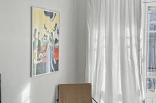 Poltrona junto à janela com cortinas brancas e luz natural na sala de estar.