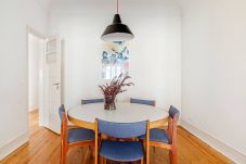 Mesa de jantar redonda com cadeiras e candeeiro suspenso num espaço luminoso e minimalista.